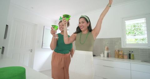 Multiethnic women celebrating st patrick's day with green cocktails in sunny modern kitchen