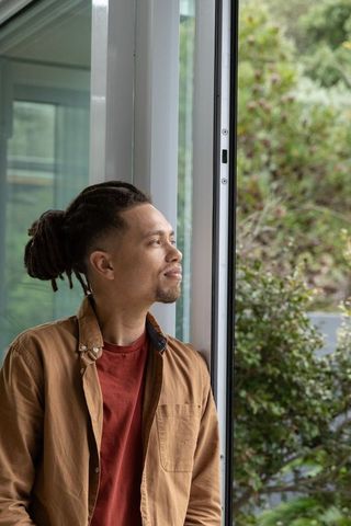 Contemplative african american man standing by sliding glass door gazing at green garden