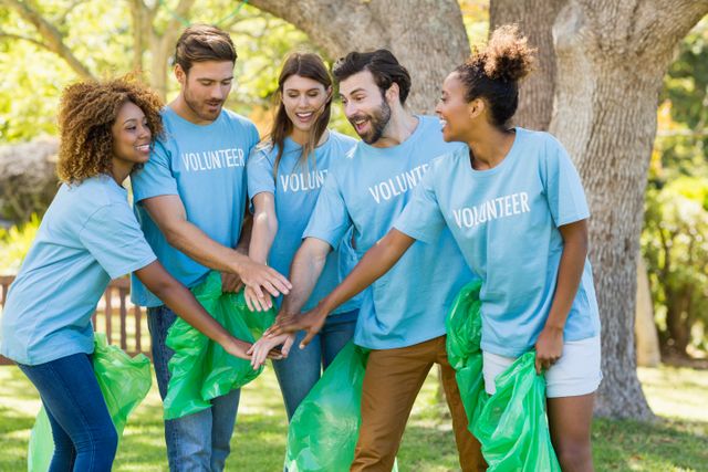Diverse group of volunteers stacking hands in unity while participating in a park cleanup. Ideal for promoting community service, environmental conservation, teamwork, and social responsibility initiatives. Perfect for use in campaigns, advertisements, and articles related to volunteer work and community engagement.