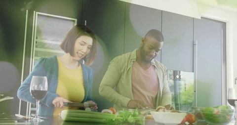 Couple chopping vegetables and preparing meal on sunlit kitchen island with wine and fresh produce