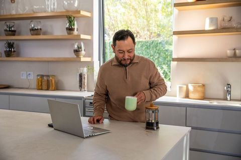 Mature asian man working from home with laptop and coffee at modern kitchen island