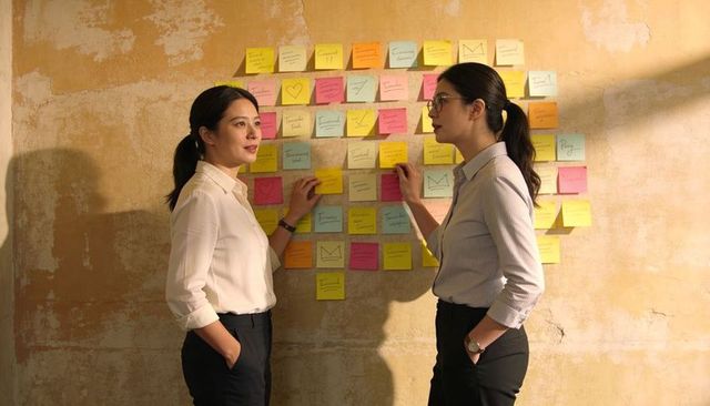 Two women collaborating and planning with colorful sticky notes on textured plaster wall