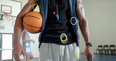 Basketball coach holding ball checking smartphone wearing whistle and smartwatch on indoor court