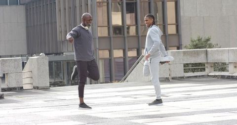 Diverse men stretching on urban rooftop plaza before outdoor workout with headphones