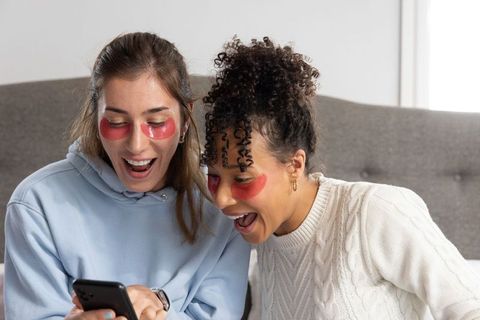 Friends laughing and reacting to phone while wearing under-eye gel patches and cozy sweaters