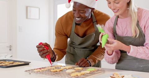 Happy couple icing christmas cookies with colorful frosting and santa hats