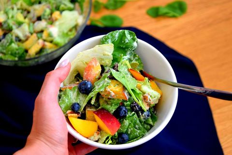 Hand holding fresh peach blueberry avocado salad bowl with creamy dressing