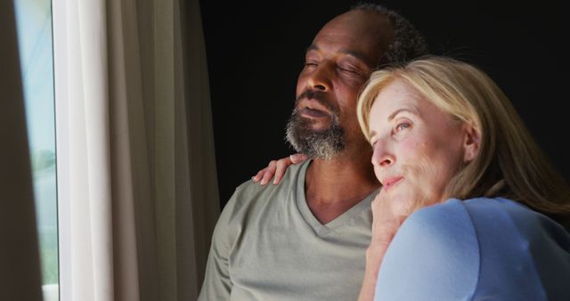 Biracial senior couple embracing each other while looking out of the window at home. staying at home in self isolation in quarantine lockdown