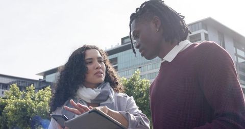 Urban professionals discussing tablet and smartphone while collaborating outdoors in plaza