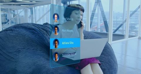 Asian woman using holographic contact list while working on laptop in coworking lounge