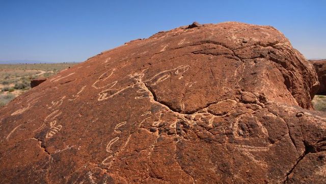 Ancient petroglyphs carving on red sandstone boulder overlooking arid plain with dirt track