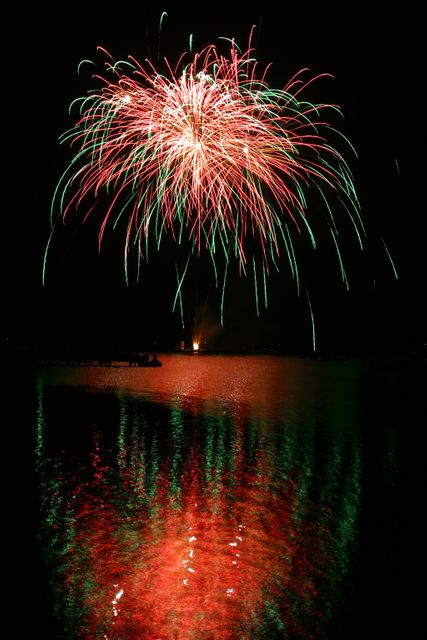 Brilliant green and red fireworks burst in the night sky and reflect beautifully on a calm lake. Great for illustrating festive events, holiday celebrations, New Year's Eve, or Fourth of July. Suitable for use in advertisements, event flyers, greeting cards, or magazine covers stressing celebrations and fireworks displays.