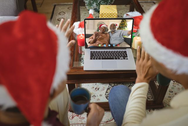 Diverse couple with santa hats having video call with happy african american couple. Christmas, celebration and digital composite image.