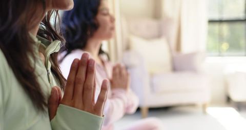 Diverse women meditating at home with palms pressed to chest in soft natural window light