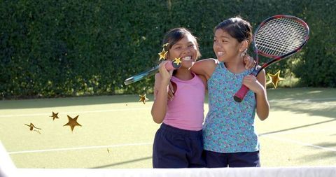 Smiling young girls celebrating tennis win on sunny court with rackets and friendship