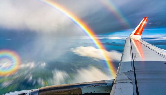 Airliner wing reflecting vivid double rainbow and spectacular glory over cloudscape