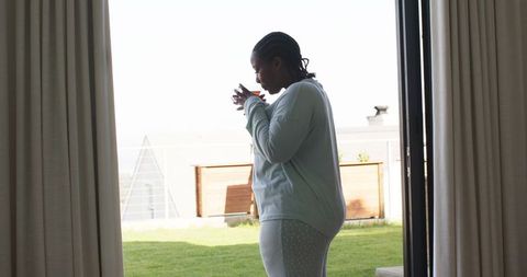 Mid-adult african american woman standing in doorway sipping tea on sunlit terrace