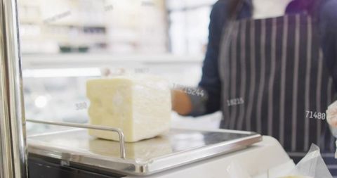 Weighing Cheese Block on Digital Scale Behind Deli Hygiene Screen, Staff in Striped Apron