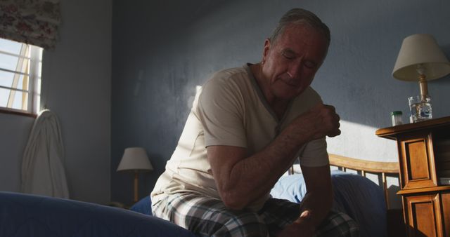 Elderly man experiencing shoulder pain while sitting on bed at home - Download Free Stock Images Pikwizard.com