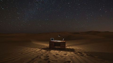 Desk and Laptop Under Starry Desert Sky at Night