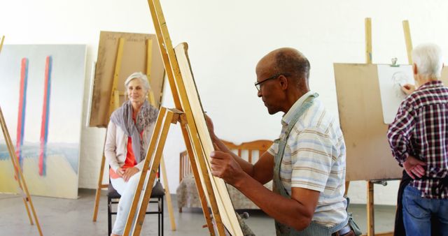 Elderly artists painting at life drawing class in studio. Elderly man focusing on painting while other individuals work on their art. Ideal for use in articles related to senior activities, creative aging, art education, and lifestyle of retired individuals engaging in artistic hobbies.