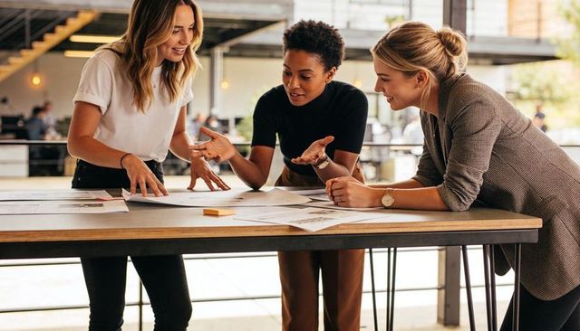 Three female professionals collaborating over project plans at tall table in modern coworking space