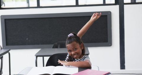 Joyful african american girl raising hand in classroom