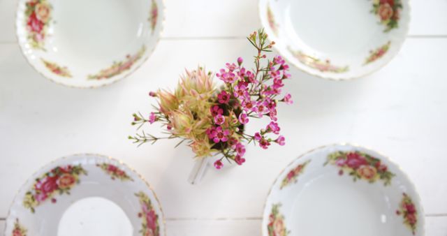 A bouquet of small pink flowers is arranged in a teacup, surrounded by other empty teacups with floral designs, with copy space. This setup creates a delicate and charming atmosphere, ideal for a vintage-themed tea party or a springtime table setting.