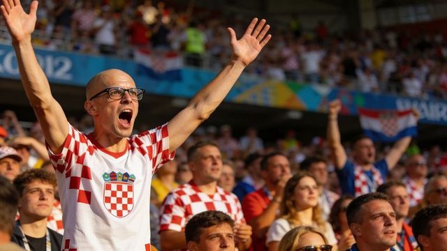 Bald man with glasses cheering among croatian fans in sunlit stadium celebration