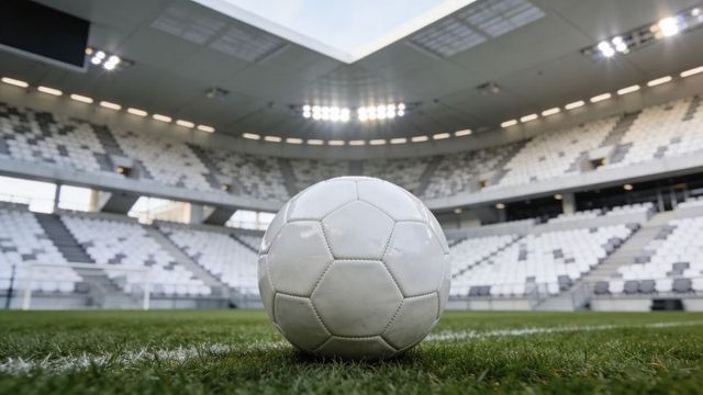 Close-up white soccer ball sitting on green turf inside empty stadium under floodlights
