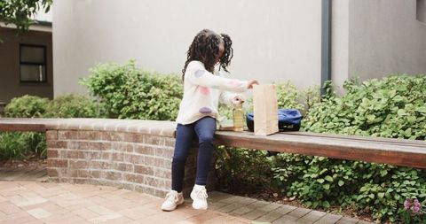 African american girl with paper lunch bag in school courtyard