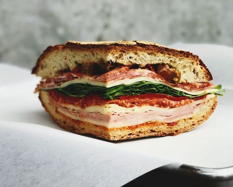 Rustic sourdough deli sandwich stacked with ham, salami, provolone, spinach and peppers