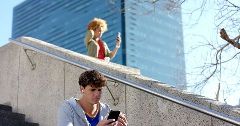 Urban commuters using smartphones on concrete plaza stairs wearing earbuds and holding coffee