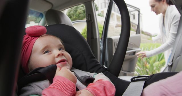 Parent ensuring child safety by securely placing toddler in car seat before driving. Suitable for illustrating parenting tips, travel safety guides, family transport, and car safety education.