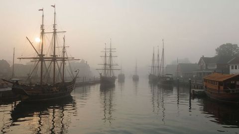 Serene morning with tall-masted ships in foggy harbor