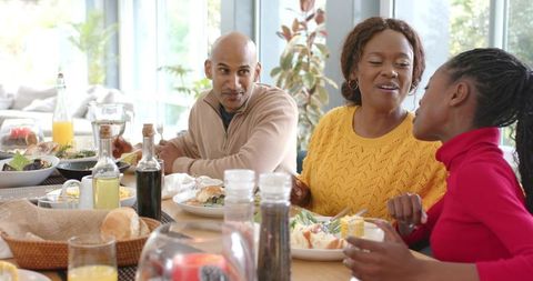 Family Sharing Sunlit Brunch at Home, Laughing, Passing Bread and Orange Juice