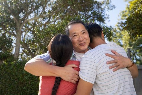 Asian Family Embracing in Sunny Backyard Garden with Lush Trees