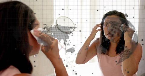Adjusting earbuds in vanity mirror with dotted world map overlay, personal grooming moment