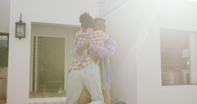 Young couple celebrating outside their new house in bright sunshine, sharing a loving embrace. Perfect for use in real estate, homeownership promotions, relationship counseling, and happy lifestyle themes.