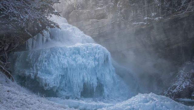 Frozen waterfall cascading in narrow gorge with dramatic blue ice formations and mist