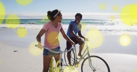Couple Enjoys Cycling on Sandy Beach Amidst Yellow Bokeh