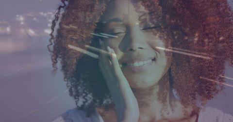 Dreamy double-exposure portrait of smiling woman with curly hair resting hand on cheek