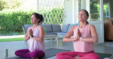 Diverse women meditating together on sunlit patio with yoga mats and water bottle