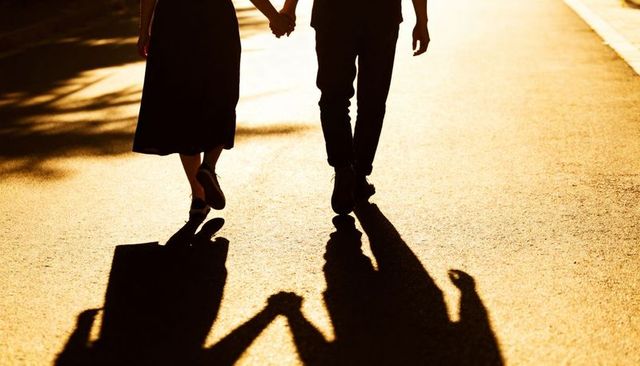 Golden sunset couple walking hand in hand casting long dramatic shadows on pavement
