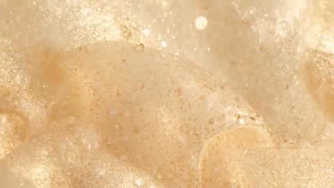 Macro Video of Beige Foam Collapsing Microbubbles with Warm Shimmering Bokeh