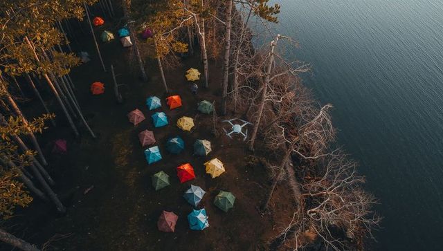 Drone capturing colorful lakeside tent camp among tall pines at twilight