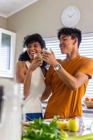 Multiracial couple toasting fresh green juice in bright modern kitchen