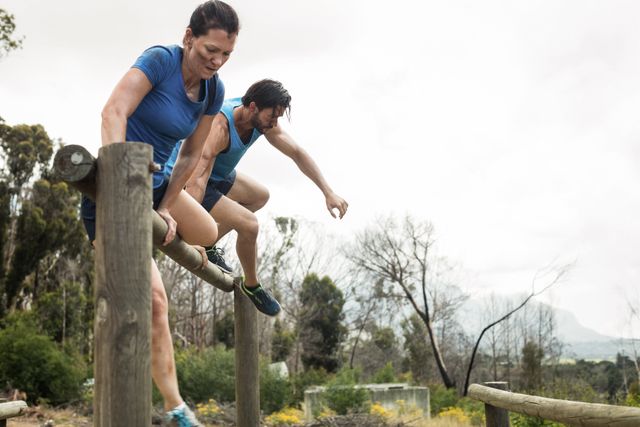 Couple participating in an outdoor boot camp, jumping over hurdles on an obstacle course. Ideal for use in fitness and health promotions, teamwork and training programs, or advertisements for outdoor adventure activities. Highlights physical activity, teamwork, and a healthy lifestyle.