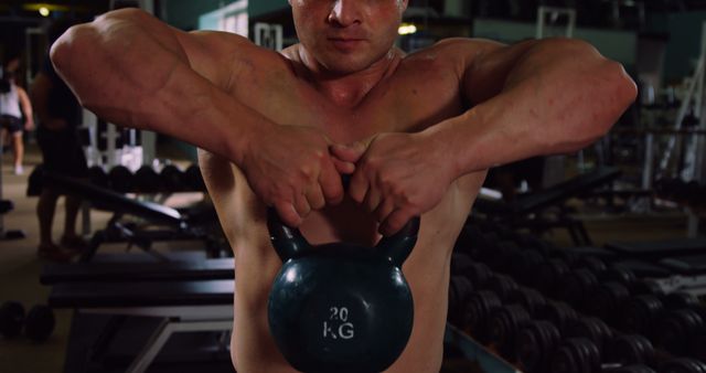 Focused caucasian muscular man lifting black kettlebell in dark gym - Download Free Stock Photos Pikwizard.com