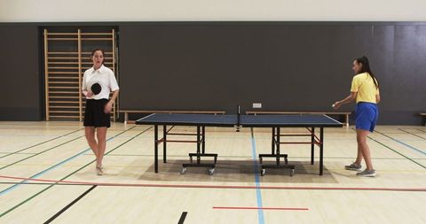 Women Engaging in Table Tennis Match at Gymnasium